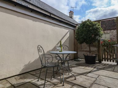 A small outdoor patio with a metal table and two chairs with a bottle and glasses and a potted tree near a wooden gate at Garden Cottage in Upottery