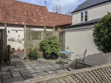 A patio with a small round metal table and two chairs with a bottle on the table and plants around at Garden Cottage in Upottery