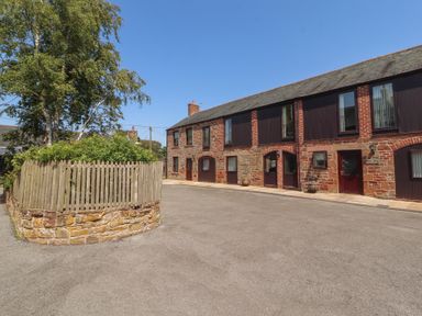 A row of buildings with a fence and trees at The Hayloft near Wigton