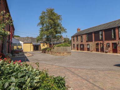 An outdoor courtyard with buildings and a tree at The Hayloft near Wigton