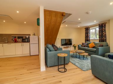 A living room with blue sofas a TV and coffee tables next to a kitchen area with white cabinets and a refrigerator at Hideaway in Great Torrington