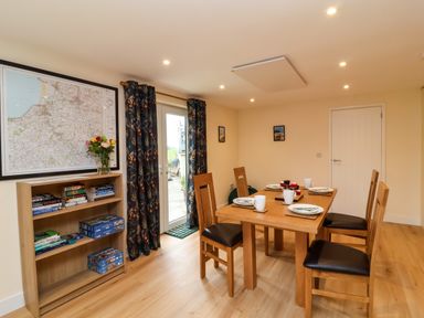 A dining room with a wooden table set for four and a bookshelf with books and games at Hideaway in Great Torrington