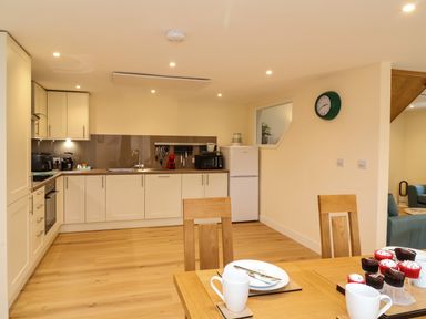 A kitchen with white cabinets wooden floor dining table with cupcakes and mugs at Hideaway in Great Torrington