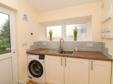 A laundry room with a washing machine sink and two windows with plants on the windowsill at Hideaway in Great Torrington