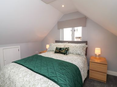 A bedroom with a bed with patterned bedding green throw and bedside tables with lamps at Hideaway in Great Torrington