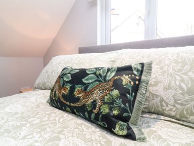 A bedroom with a bed that has floral bedding and a decorative pillow with leopard and leaf patterns at Hideaway in Great Torrington
