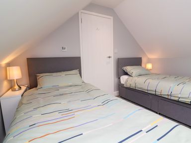 A bedroom with two single beds with striped bed covers and bedside tables with lamps at Hideaway in Great Torrington