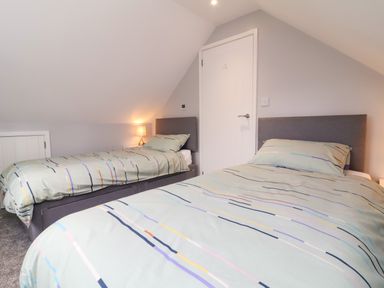 A bedroom with two single beds with striped bedding and a lit bedside lamp at Hideaway in Great Torrington