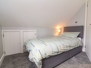 A bedroom with a grey bed a side table with a lamp and storage doors under a sloped ceiling at Hideaway in Great Torrington