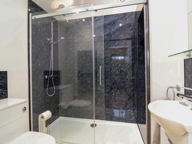 A bathroom with a glass enclosed shower with black marble walls a white sink and toilet at Hideaway in Great Torrington