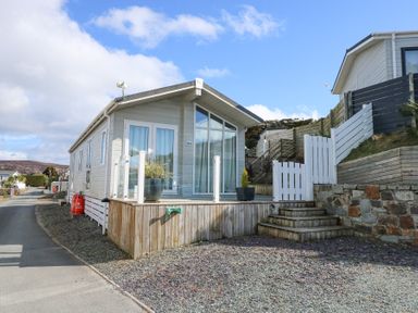 A small modern house with large windows and a wooden deck with potted plants at Ocean Breeze in Abersoch