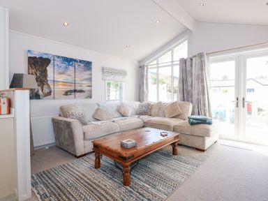 A living room with a beige sectional sofa wooden coffee table and large windows at Ocean Breeze in Abersoch