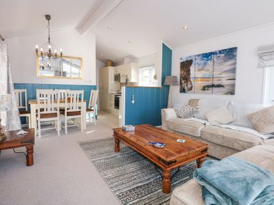 A living room with couches wooden coffee table dining table and kitchen area at Ocean Breeze in Abersoch