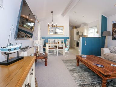 A living room with a dining table chairs wooden coffee table and a mounted television at Ocean Breeze in Abersoch