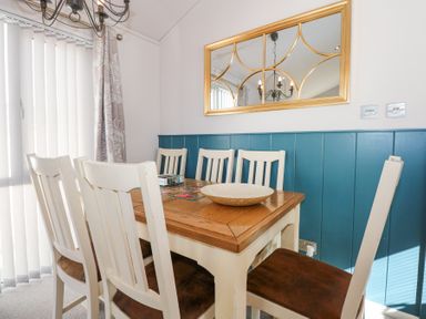 A dining room with a wooden table and six white chairs with brown seats at Ocean Breeze in Abersoch