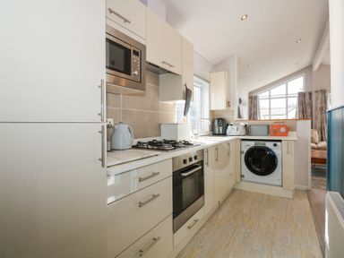 A kitchen with cabinets microwave oven utensils and washing machine at Ocean Breeze in Abersoch