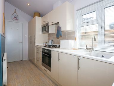 A kitchen with white cabinets a microwave oven a gas stove a sink under a window and a door at Ocean Breeze in Abersoch