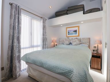 A bedroom with a bed a painting two lamps curtains and cushions at Ocean Breeze in Abersoch