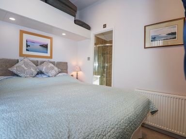 A bedroom with a bed green bedspread and two framed pictures on the walls at Ocean Breeze in Abersoch