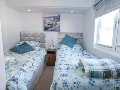 A bedroom with two single beds a small wooden nightstand and a window at Ocean Breeze Abersoch