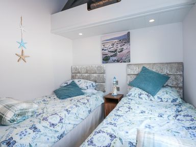 A bedroom with two single beds with floral bedding and pillows and a small bedside table with a lighthouse decoration at Ocean Breeze in Abersoch