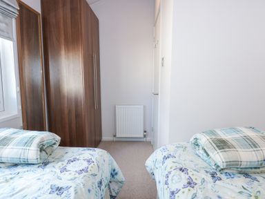 A bedroom with two single beds and a wooden wardrobe at Ocean Breeze in Abersoch