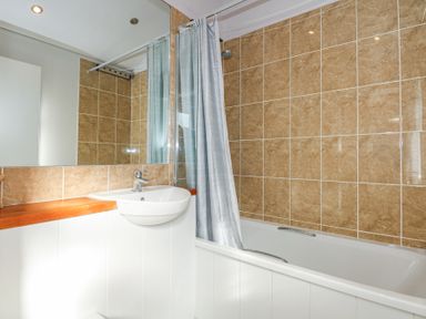 A bathroom with a bathtub shower combination a sink with wooden countertop and beige tiled walls at Ocean Breeze in Abersoch