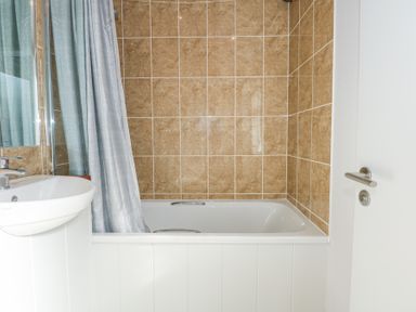 A bathroom with a bathtub a shower curtain a sink and tiled walls at Ocean Breeze in Abersoch