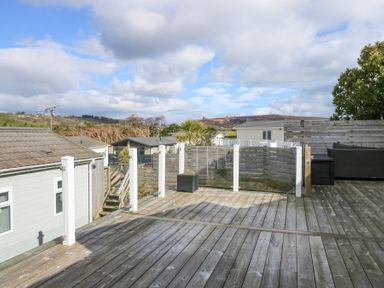 A wooden deck with glass railing overlooking nearby houses and hills at Ocean Breeze in Abersoch