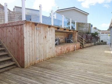 An outdoor wooden deck with a built-in seating area and stairs leading up to a house at Ocean Breeze in Abersoch