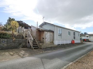 A white mobile home with wooden stairs and storage by a paved road with gas cylinders nearby at Ocean Breeze in Abersoch
