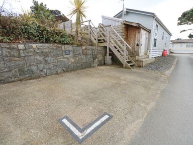 A parking space marked B16 beside a stone wall and a wooden staircase leading to a raised walkway at Ocean Breeze in Abersoch