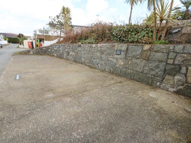 An empty parking space next to a stone wall with plants above at Ocean Breeze in Abersoch