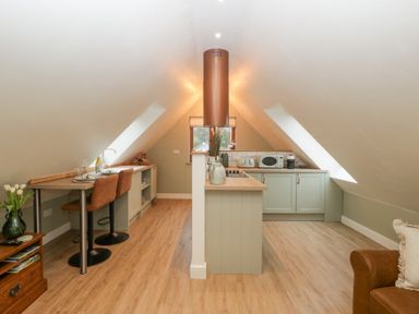 A kitchen with a central island under sloped ceilings with two brown bar stools and a brown leather armchair at Pheasants Rise Apartment in Ross-On-Wye