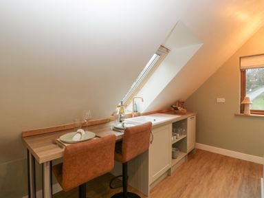 A kitchen area with a wooden countertop dining table set for two under a slanted ceiling window at Pheasants Rise Apartment in Ross-On-Wye