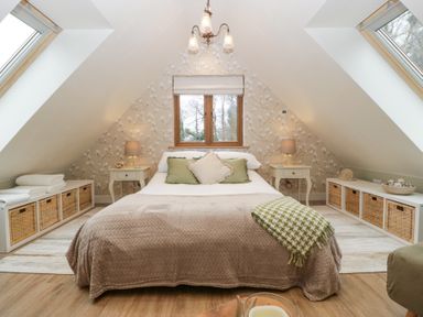 A bedroom with a bed in the center, nightstands with lamps on each side, storage baskets below skylight windows and a small window on the back wall at Pheasants Rise Apartment in Ross-On-Wye
