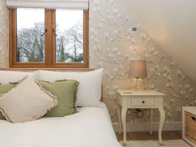 A bedroom with a bed next to a window and a bedside table with a lamp at Pheasants Rise Apartment in Ross-On-Wye