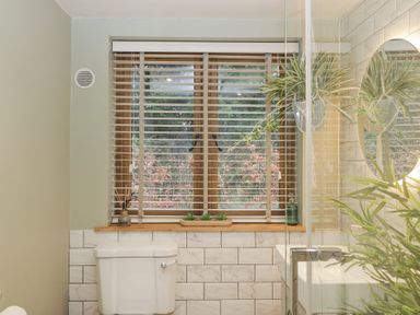 A bathroom with a toilet sink window blinds and green plants at Pheasants Rise Apartment in Ross-On-Wye