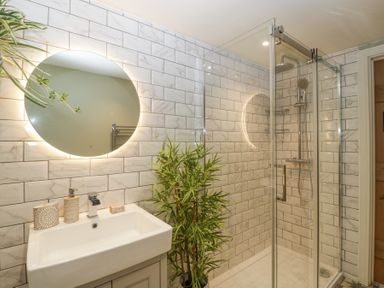 A bathroom with a sink a round mirror a shower area with glass doors and a potted plant at Pheasants Rise Apartment in Ross On Wye