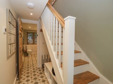 A hallway with wooden stairs and patterned tiled floor leading to a bathroom with a toilet and window at Pheasants Rise Apartment Ross-On-Wye