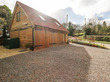 A wooden building with large wooden doors and a gravel driveway surrounded by trees and shrubs at Pheasants Rise Apartment in Ross-On-Wye