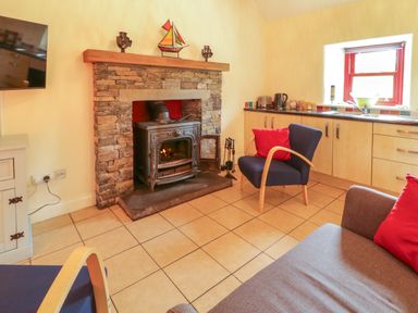 A living room with a fireplace and kitchen area at Shane's Cottage in Falcarragh, County Donegal