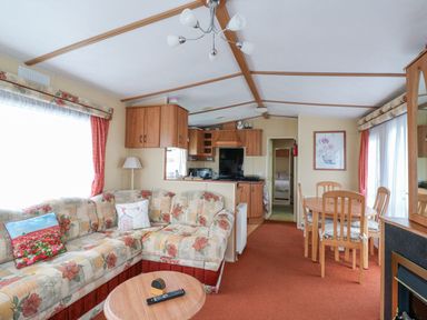 A living room with a floral patterned sofa a wooden coffee table a dining table with four chairs and a kitchen area at 120 Caravan in Hemsby