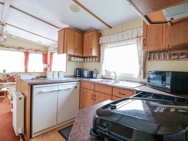 A kitchen area with wooden cabinets a sink a microwave and an appliance on the counter at 120 Caravan in Hemsby