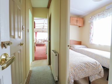 A hallway leading to a living room with a sofa and dining table and a bedroom with two single beds at 120 Caravan in Hemsby