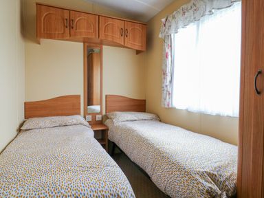 A bedroom with two single beds a wooden cupboard and a window with curtains at 120 Caravan in Hemsby