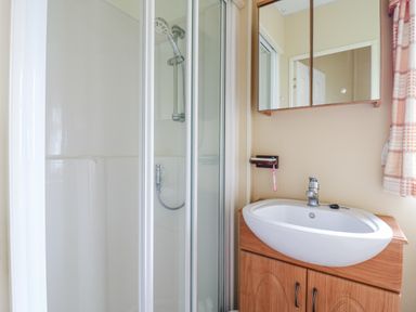 A bathroom with a shower cubicle and a sink with built in cabinet and mirrored medicine cabinet at 120 Caravan in Hemsby