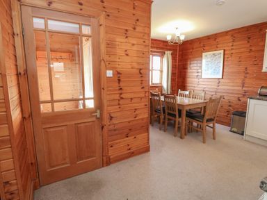 A dining area with a wooden table and six chairs near a window in a room with wooden walls at Creag Mhor Lodge Back of Keppoch near Arisaig