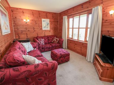 A living room with wooden panel walls red sofas a red ottoman a television on a wooden stand and a large window at Creag Mhor Lodge Back of Keppoch near Arisaig