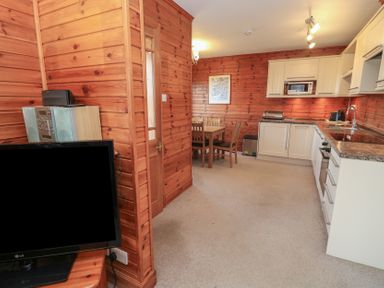 A kitchen and dining area with wooden walls a dining table with chairs white cabinets and a television at Creag Mhor Lodge Back of Keppoch near Arisaig
